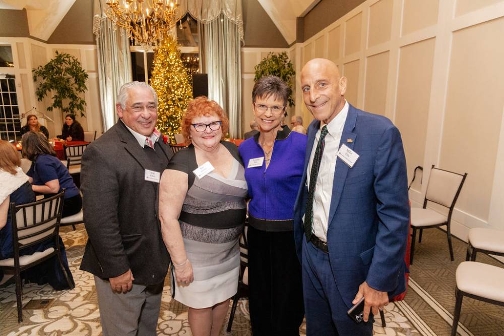 Four holiday reception guests, standing together and smiling at camera